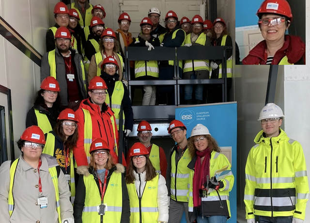 Around 20 people wearing high vis vests and red helmets stand smiling at a flight of industrial stairs, by a roll up with ESS branding