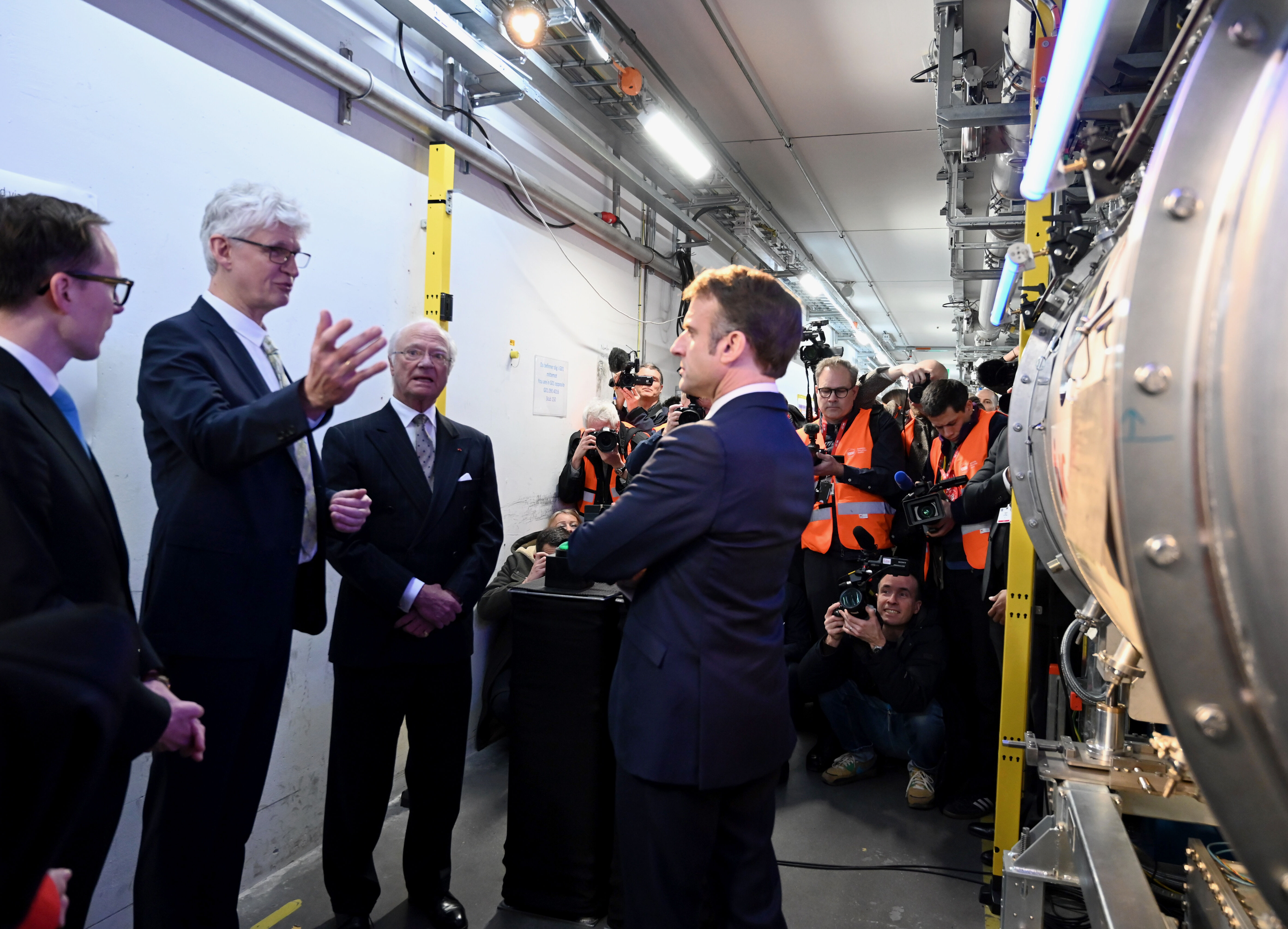 DG Helmut Schober in a tunnel with the accelerator on the right,  explains to HRH The King and President Macron about how a particle accelerator works