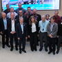25 members of the LENS meeting stand in front of a screen in the atrium of the ESS offices